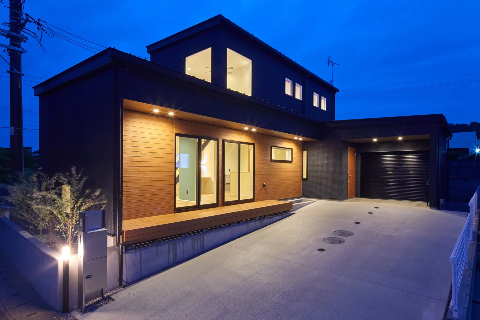 夕暮れに灯りがともるオートバイガレージのある住宅の外観